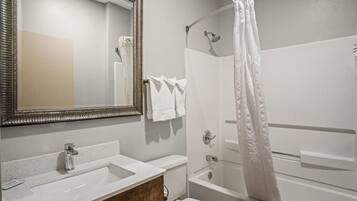 A bathroom with a large mirror, a sink, a toilet, and a shower.