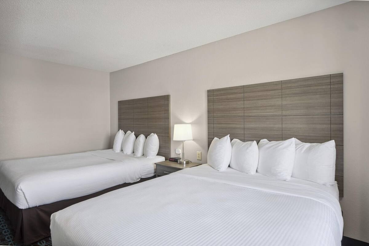 A hotel room with two single beds, a nightstand with a lamp, and a headboard with a light fixture.