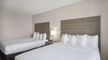 A hotel room with two single beds, a nightstand with a lamp, and a headboard with a light fixture.