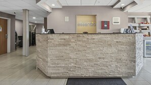 A reception desk with a stone-textured counter, a sign reading "SONESTA ESSENTIA," and a refrigerator in the background.