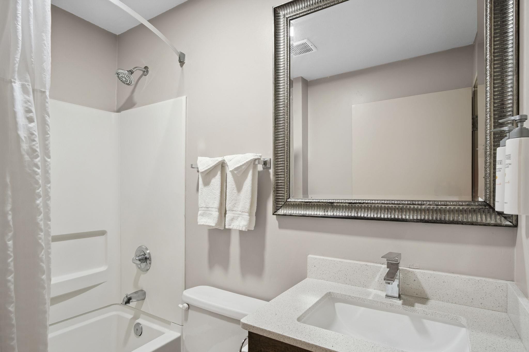 A bathroom with a shower, toilet, sink, and a large mirror.