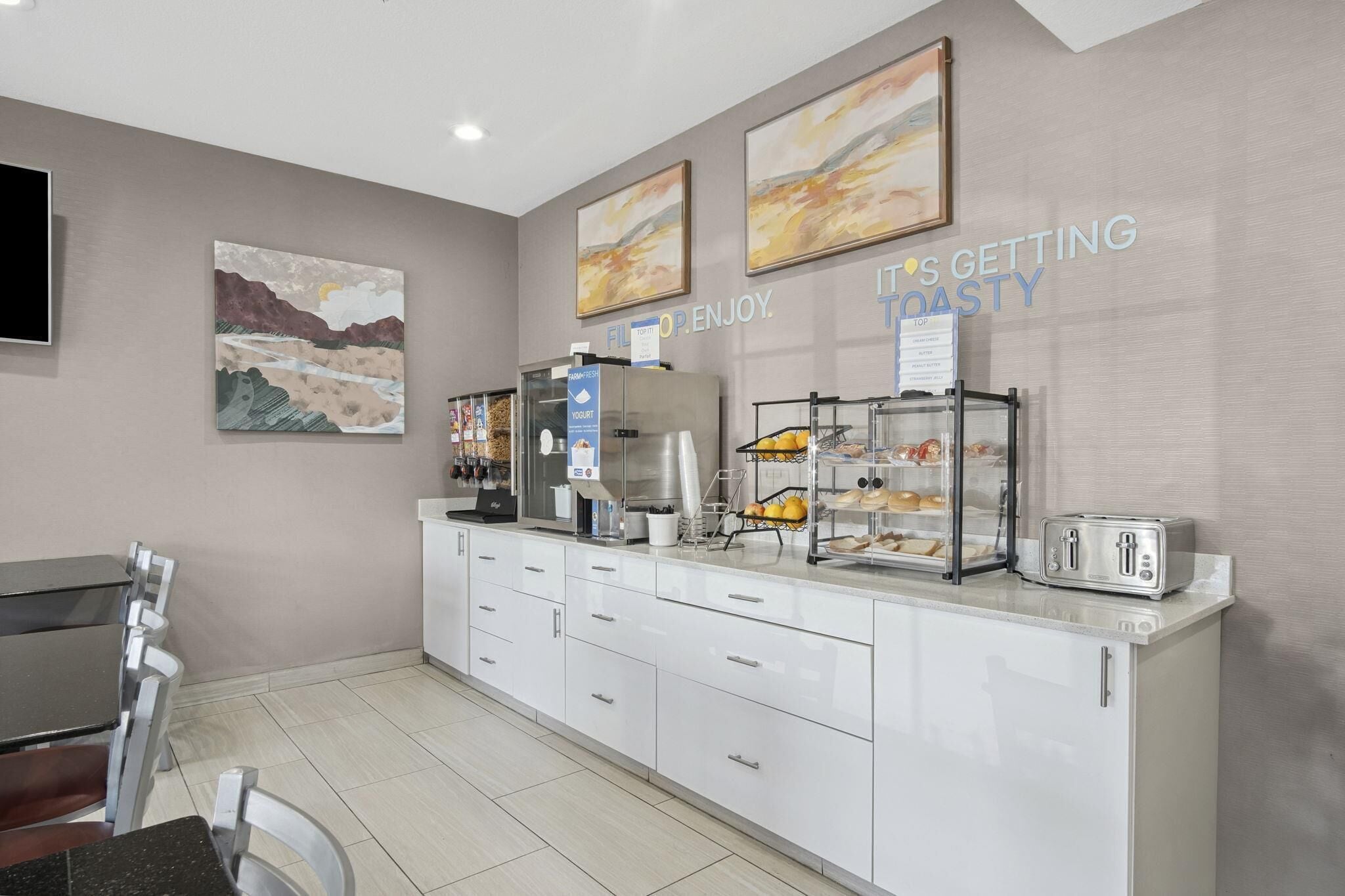 A modern hotel room with a kitchenette, a dining area, and artwork on the walls.