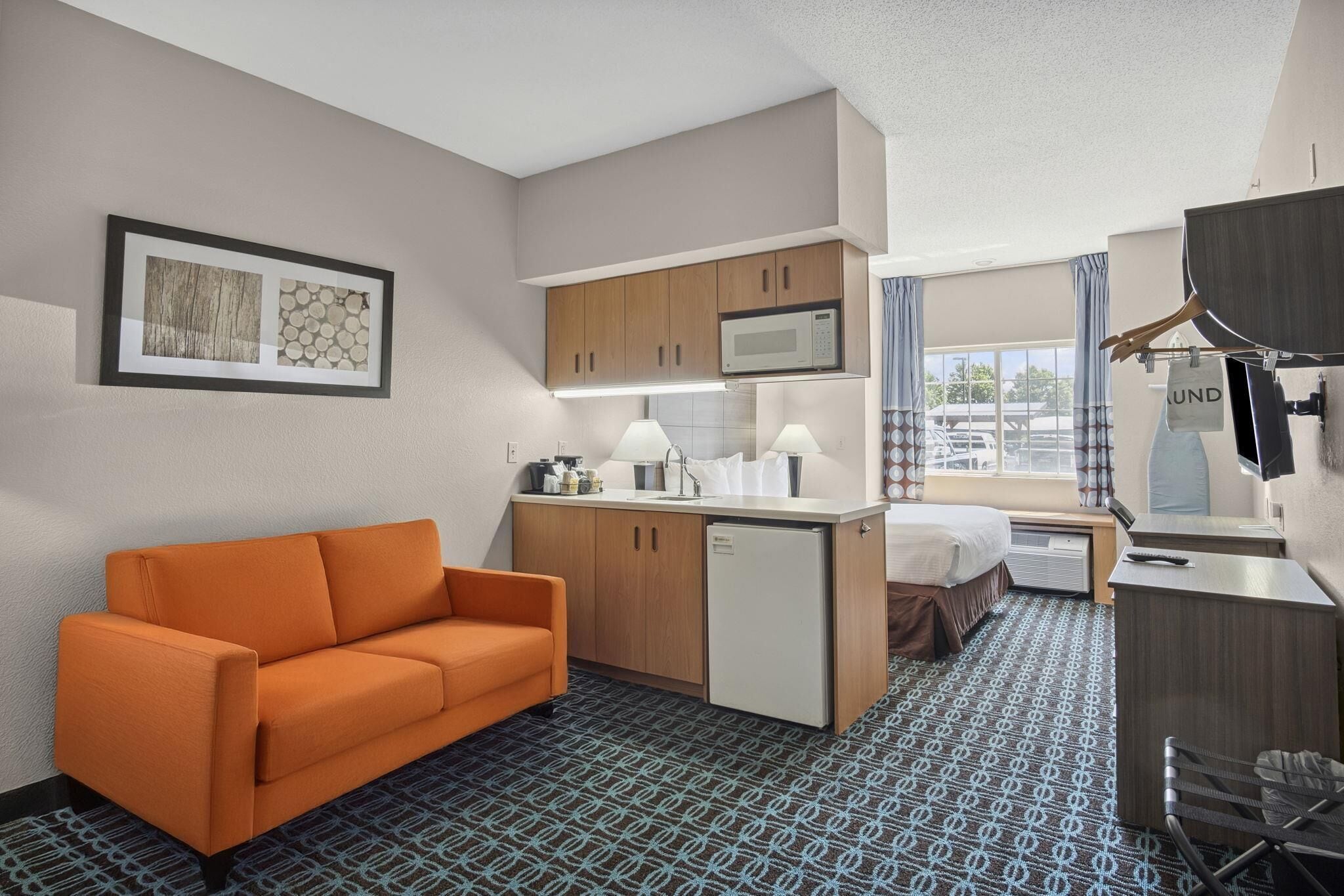 Ein kompaktes Hotelzimmer mit Küchenzeile, einer Couch, einem Bett, einem Schreibtisch und einem Fernseher.