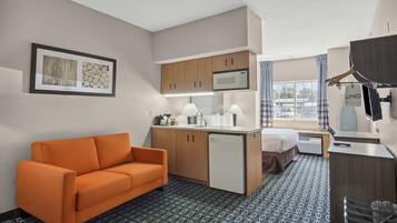 Quarto de hotel pequeno com cozinha compacta, sofá, cama, escrivaninha e televisão.