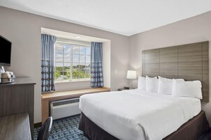 Habitación de hotel con una cama grande, un escritorio, una silla, un televisor, una ventana con cortinas y vistas al exterior.
