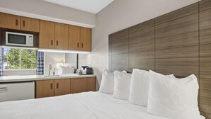 A modern hotel room with a large bed, wooden cabinets, a microwave, and a view of greenery outside.