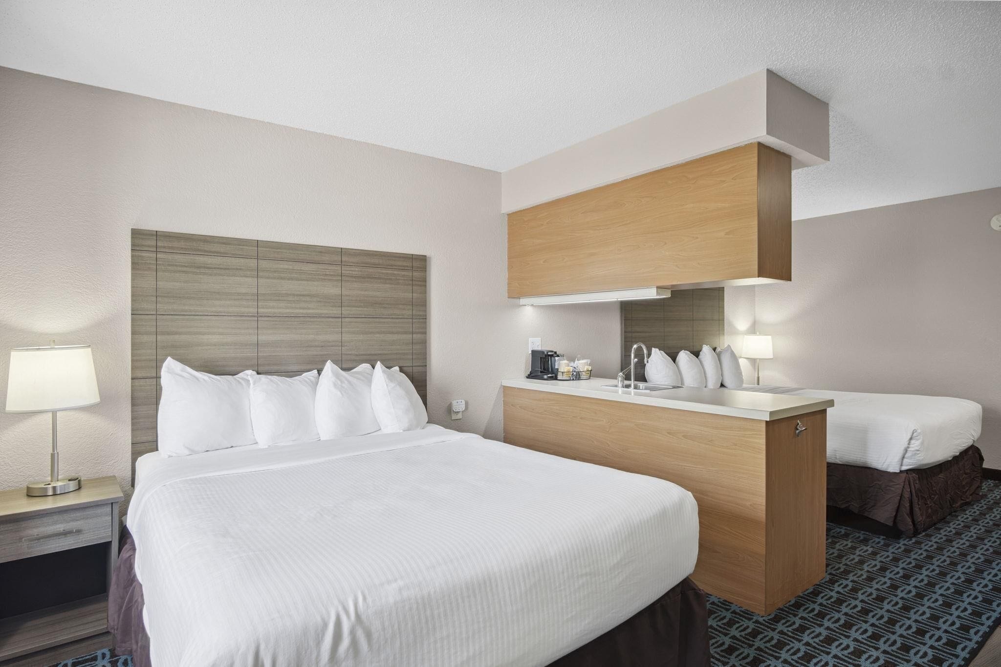 A hotel room with a large bed, a wooden headboard, a small desk with a lamp, and a bathroom mirror.