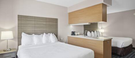 A hotel room with a large bed, a wooden headboard, a small desk with a lamp, and a bathroom mirror.