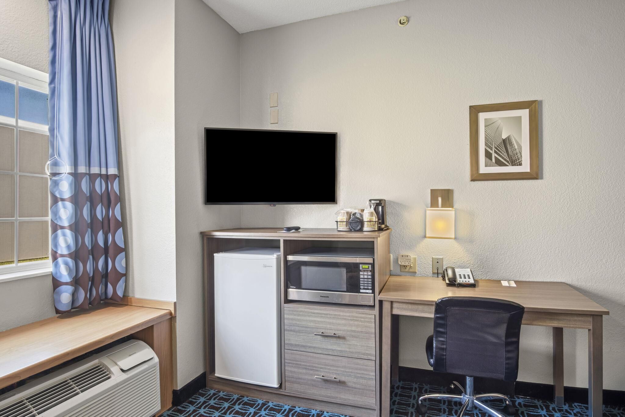 Habitación de hotel con escritorio, microondas, refrigerador y televisor.