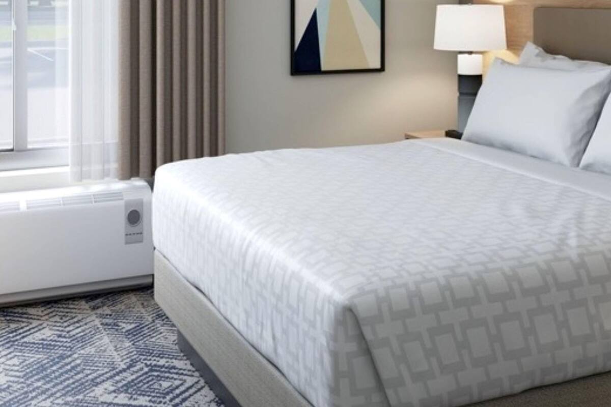 Una habitación de hotel con cama, mesita de noche, lámpara, ventana con cortinas y un cuadro colgado en la pared.