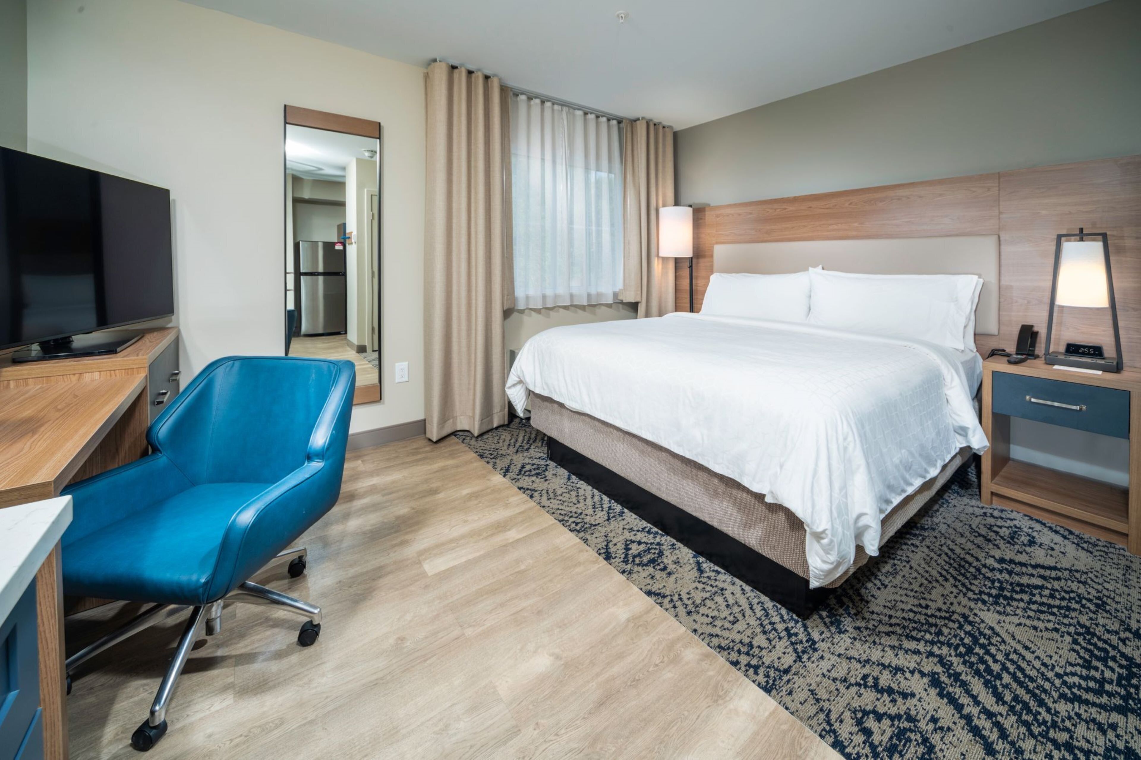 A hotel room with a bed, a desk, a chair, a TV, and a bathroom visible through an open door.