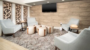 A modern lounge area with grey upholstered chairs, a flat-screen TV mounted on a wooden wall, and a patterned rug. - Candlewood Suites Charleston Mt Pleasant by IHG (Mount Pleasant)