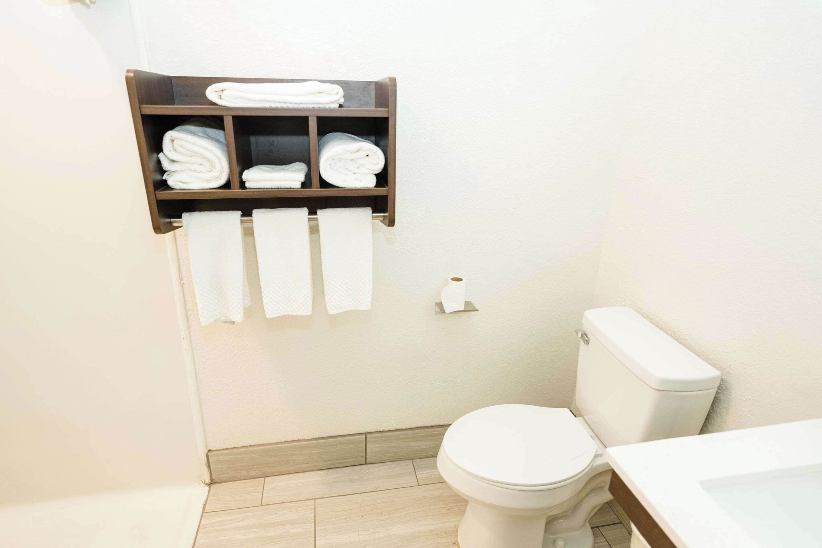 A small bathroom with a toilet, a shelf with folded towels, and a roll of toilet paper.
