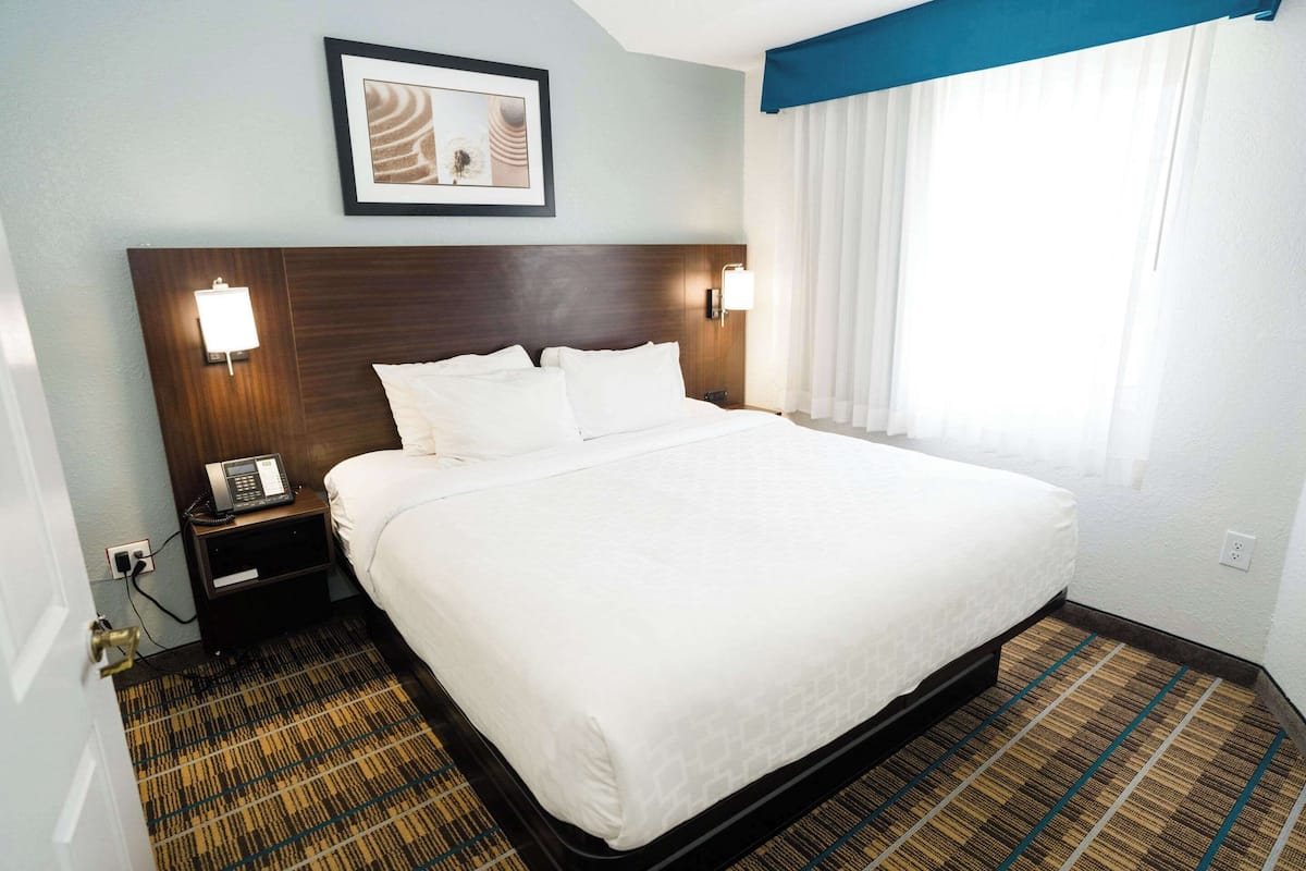 A hotel room with a large bed, a nightstand with a phone, and a wall-mounted light.