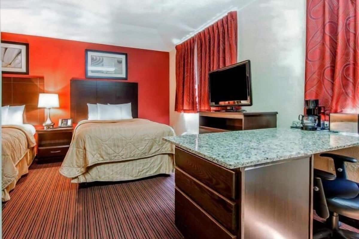 A hotel room with two beds, a TV, a desk with a coffee maker, and a red curtain.