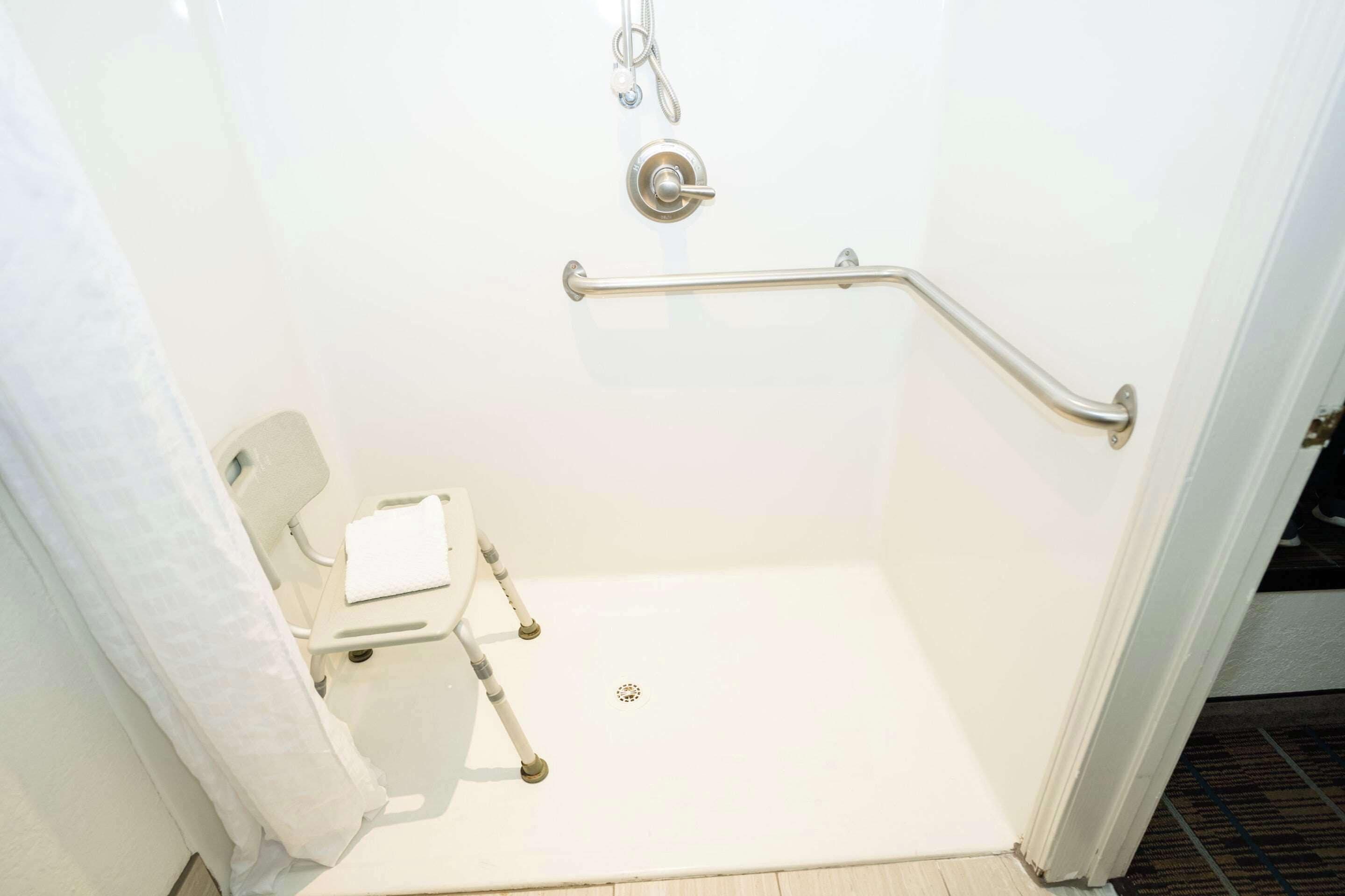 Un baño blanco con ducha, barra de apoyo y un inodoro blanco.