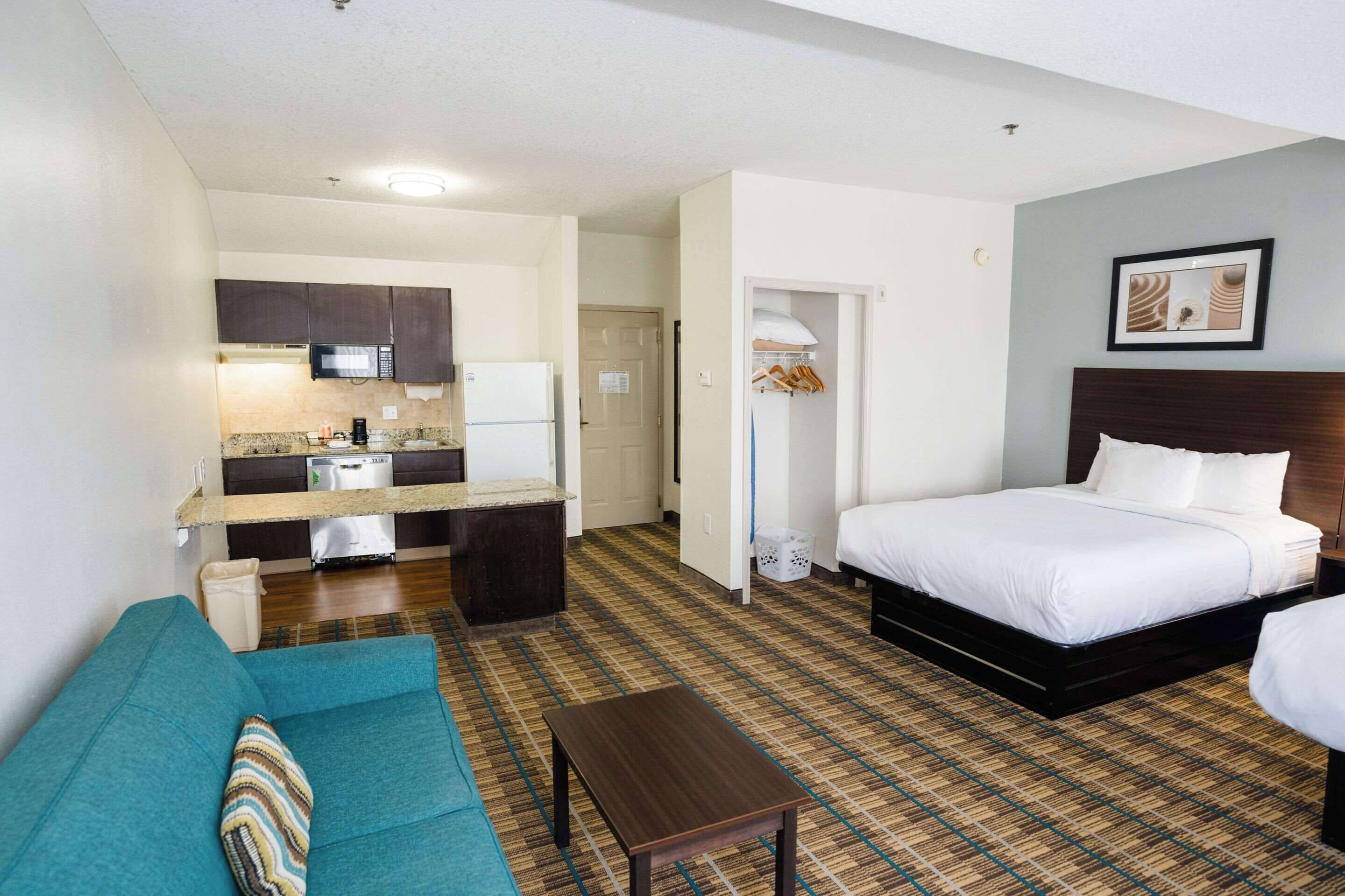 Una habitación de hotel con cama, sofá, una mesita, kitchenette y baño.