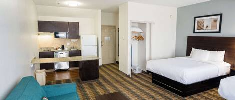 Una habitación de hotel con cama, sofá, una mesita, kitchenette y baño.