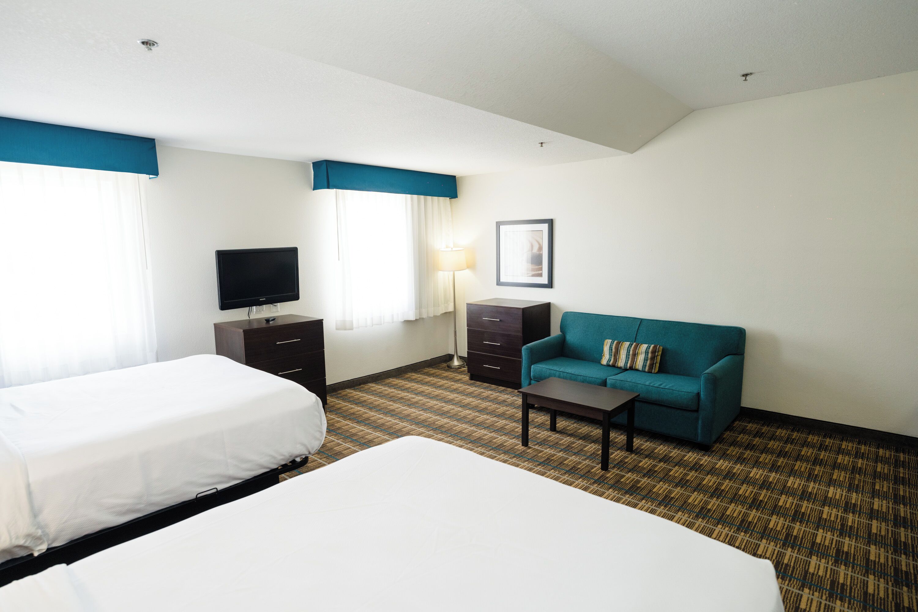 A hotel room with two beds, a TV, a desk, a lamp, and a sofa.