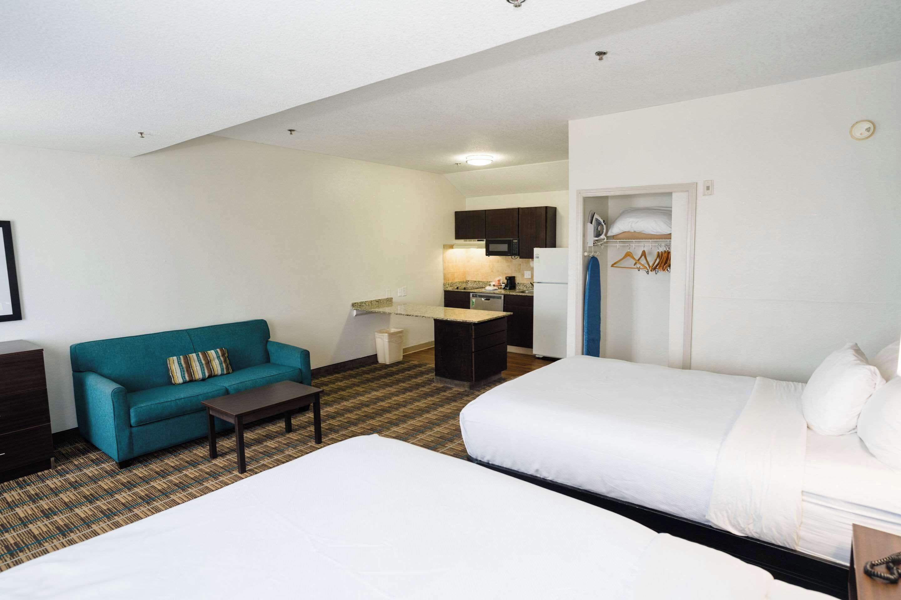 A hotel room with two beds, a sofa, a small table, a kitchenette, and a closet.