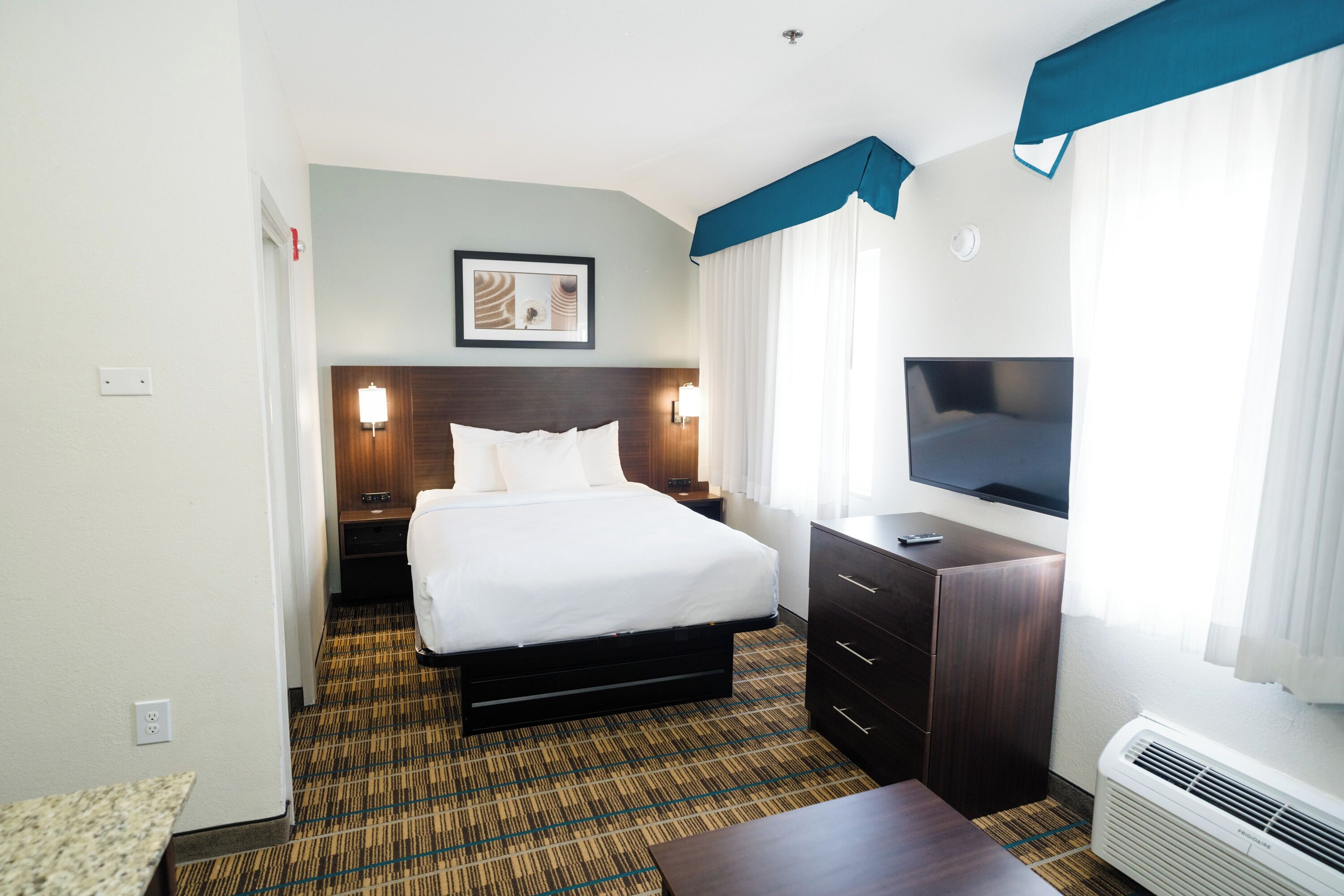 Una habitación de hotel con cama, televisión, escritorio y cómoda.