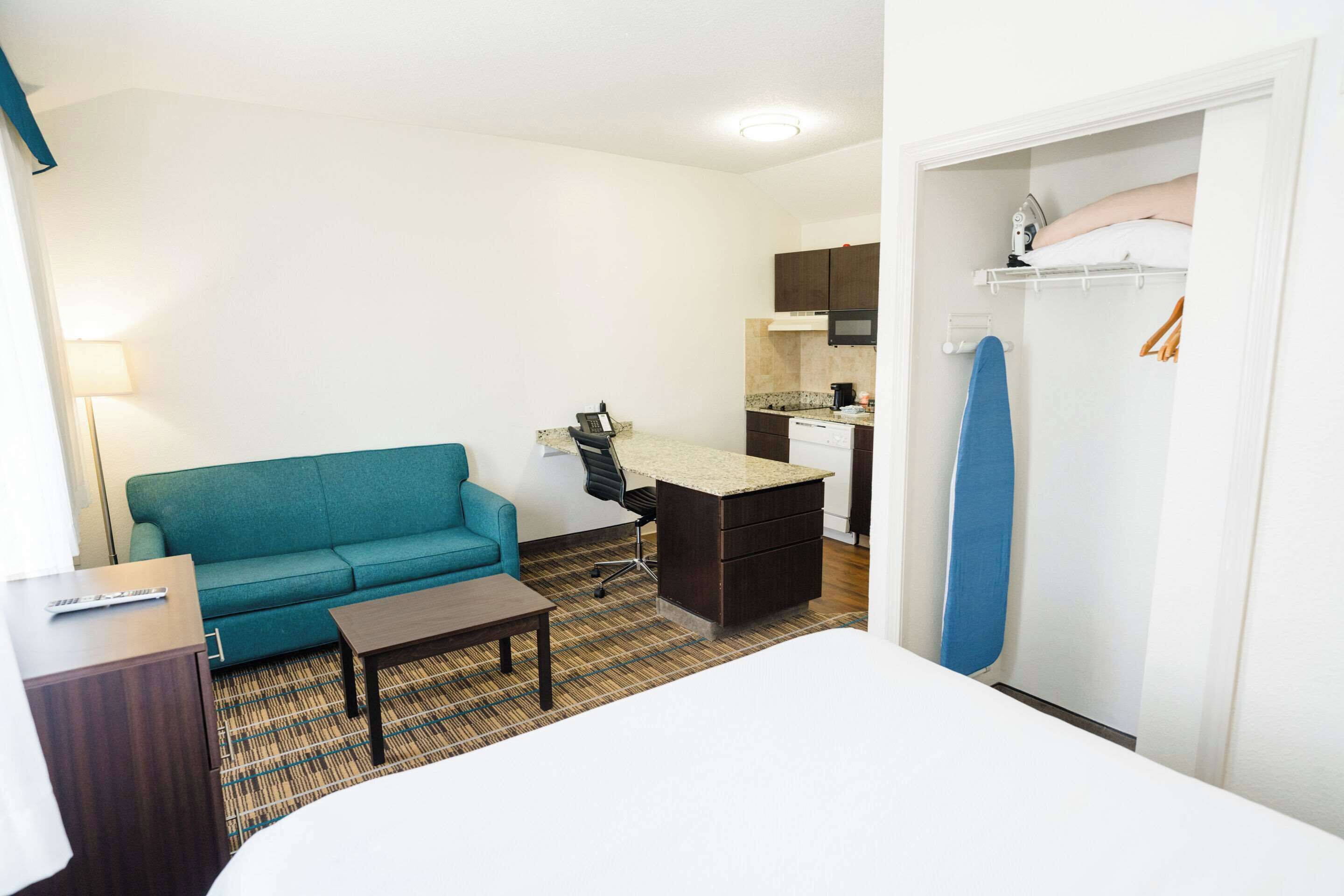 Habitación de hotel con cama, sofá, escritorio, silla, una mesita, zona de cocina y armario.