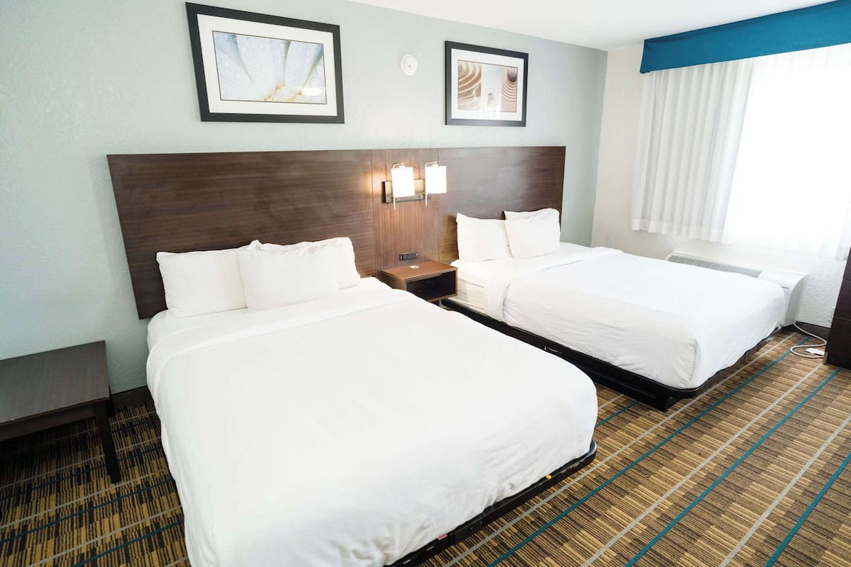 A hotel room with two beds, a headboard, wall-mounted lights, and a window with curtains.