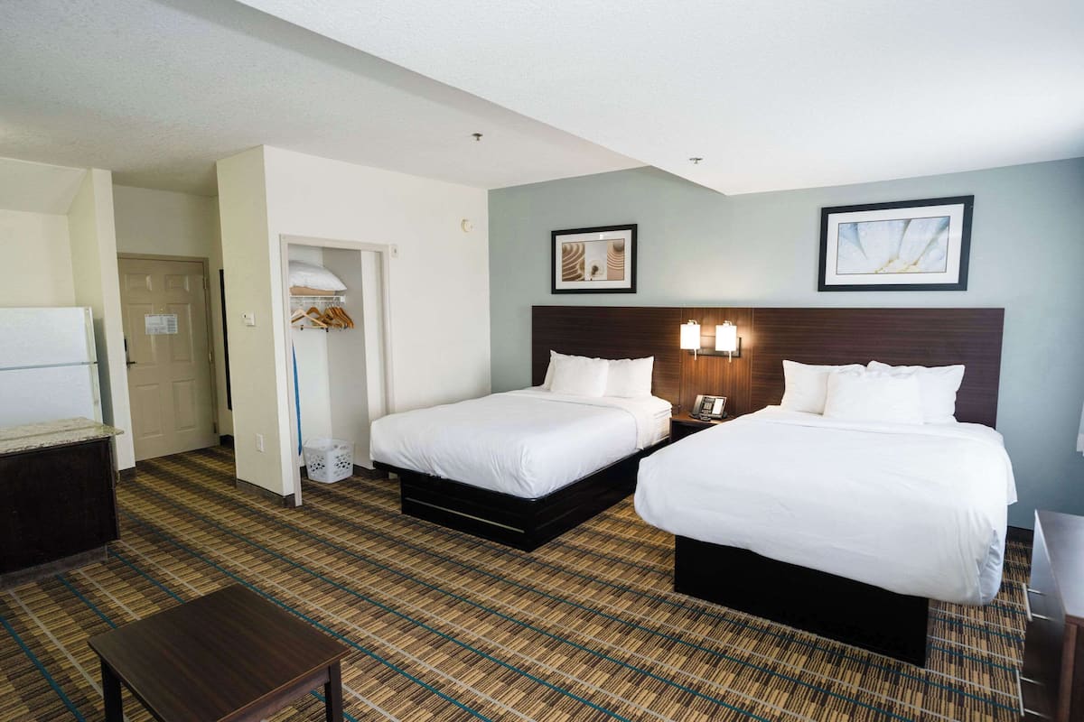 A hotel room with two beds, a small table, a wardrobe, and a door leading to another room.