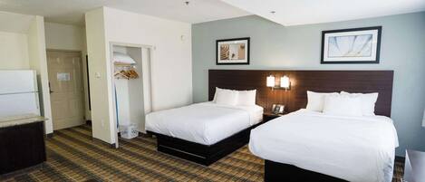 A hotel room with two beds, a small table, a wardrobe, and a door leading to another room.