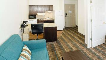 A compact living space with a kitchenette, a sofa, a coffee table, and a patterned carpet.