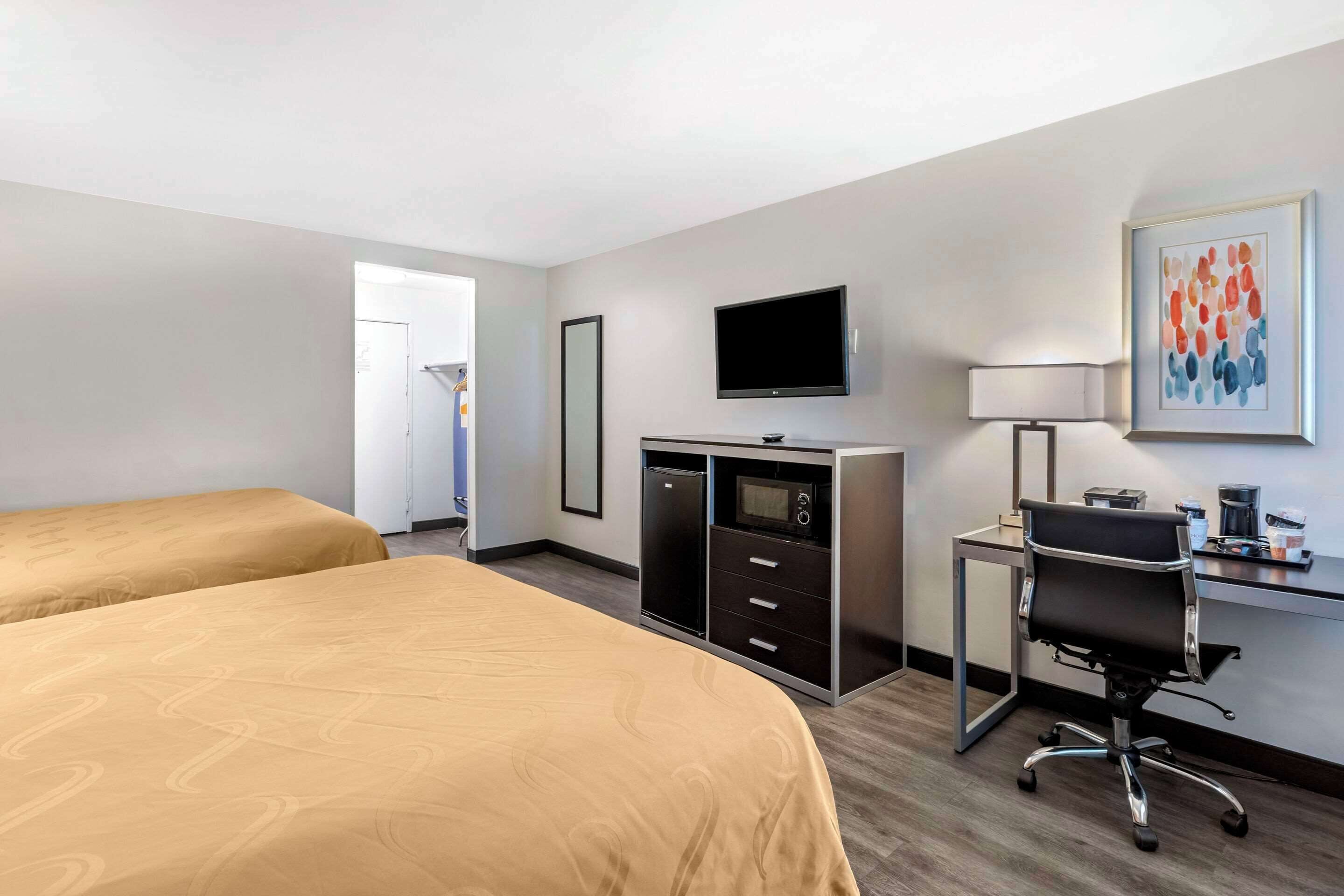 A hotel room with two beds, a desk with a computer, a TV, and a coffee maker.