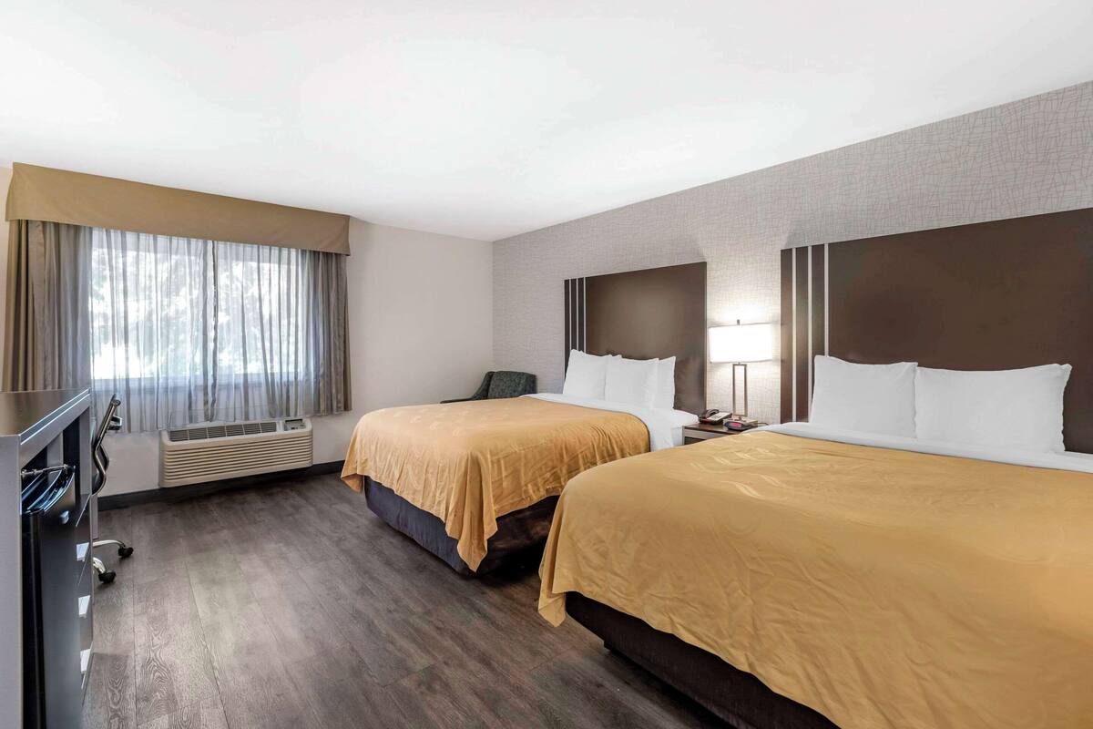 A hotel room with two beds, a desk, and a window with curtains.