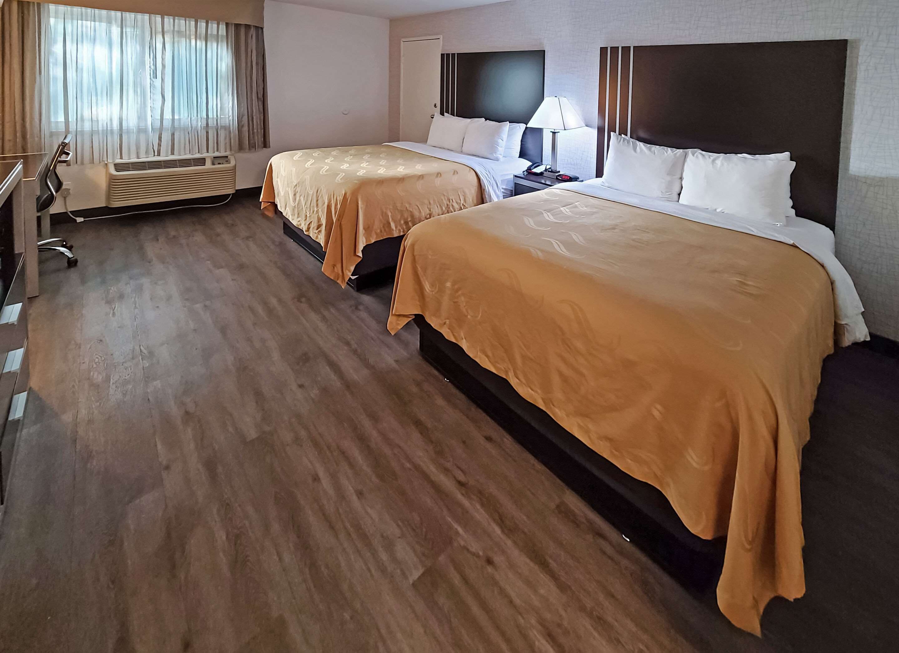 Quarto de hotel com duas camas, uma escrivaninha, uma cadeira, uma televisão e ar condicionado.