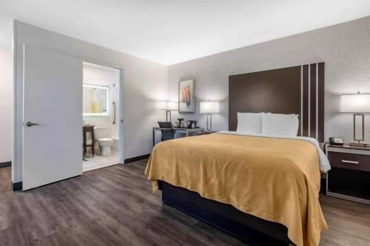 A hotel room with a bed, bedside table, lamp, and a view of the bathroom.