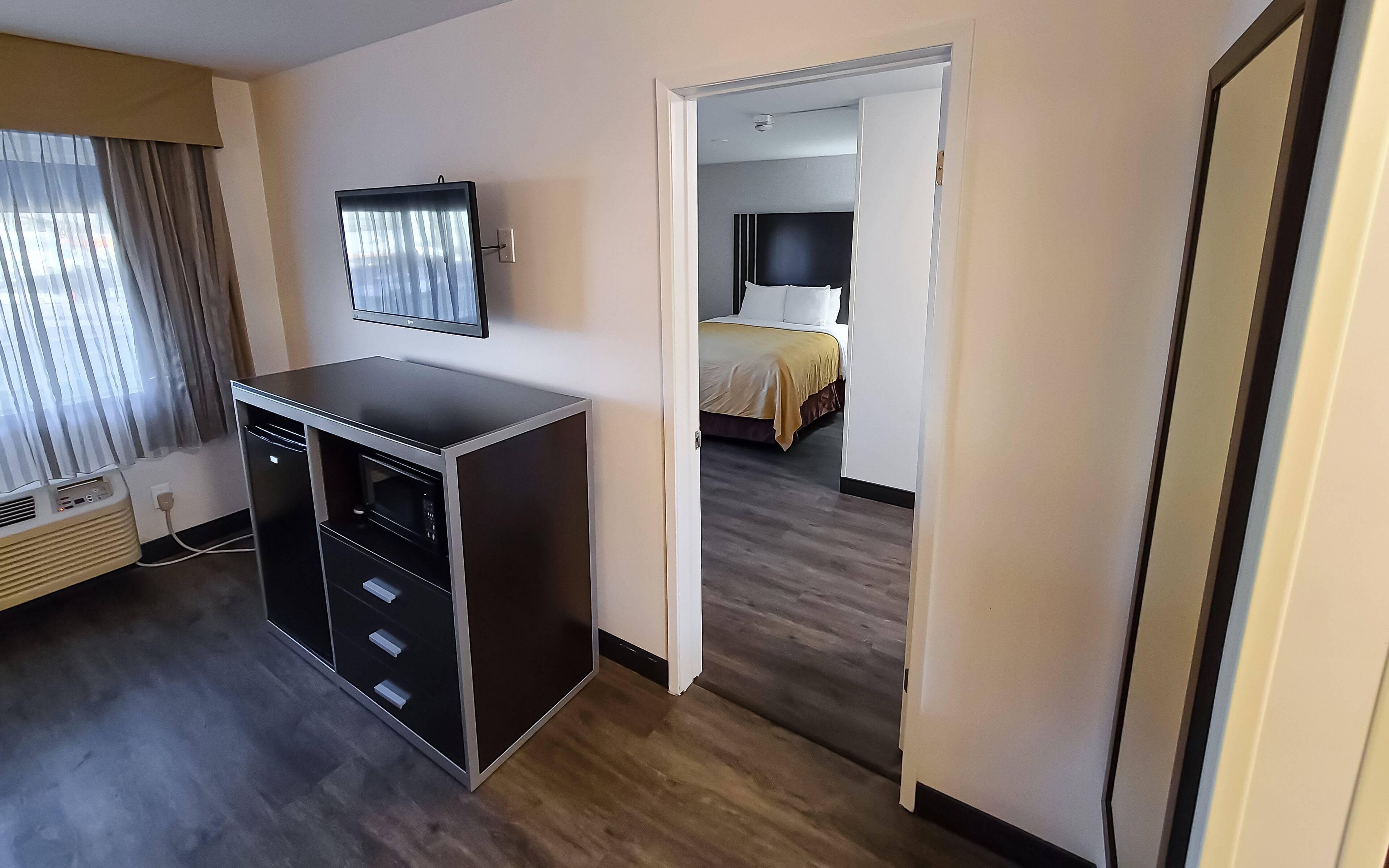 Een hotelkamer met een bureau, een televisie, een bed met een gele sprei en een houten vloer.