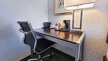 Habitación de hotel con escritorio, silla, cafetera y lámpara.
