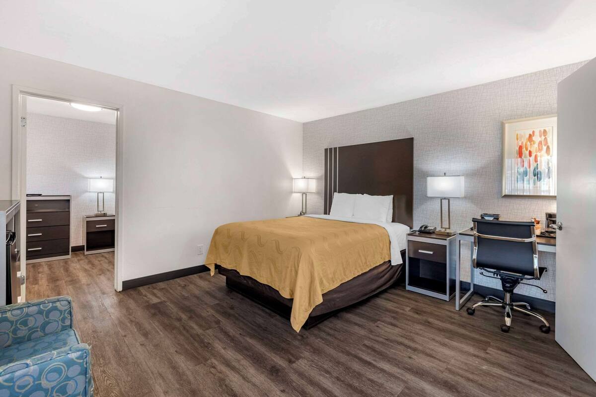A hotel room with a bed, desk, chair, and a small kitchenette.