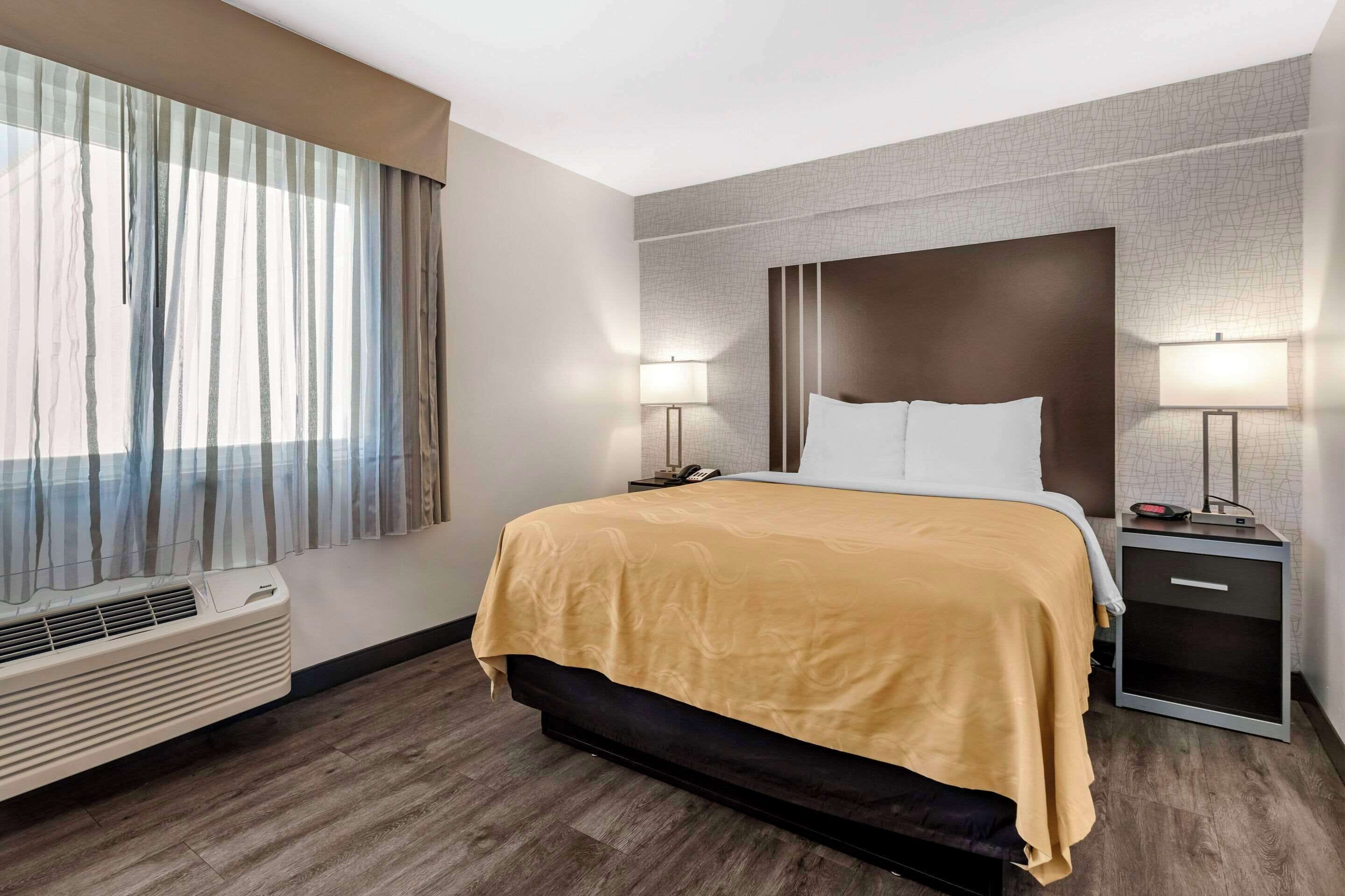 A hotel room with a large bed, two bedside tables with lamps, a heater, and a window with curtains.
