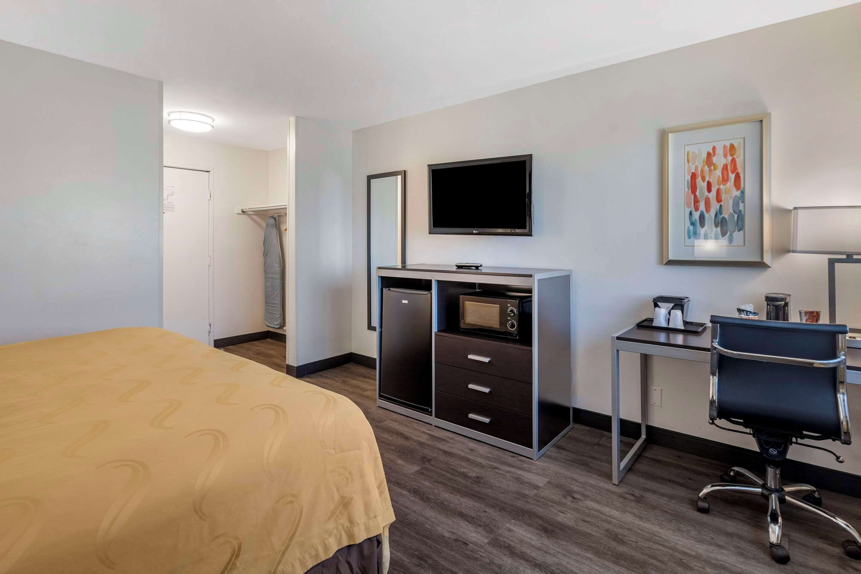 A hotel room with a bed, a desk with a computer, a TV, a microwave, and a small refrigerator.