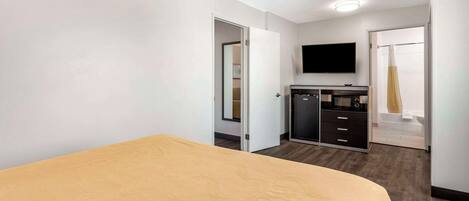 Una habitación de hotel con cama, televisor, armario y baño con ducha.