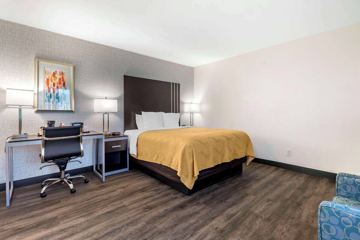 A hotel room with a bed, desk, chair, and two lamps.