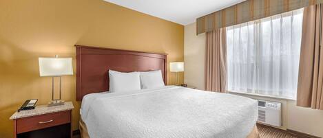A hotel room with a large bed, two bedside lamps, a nightstand with a phone, and a window with curtains.