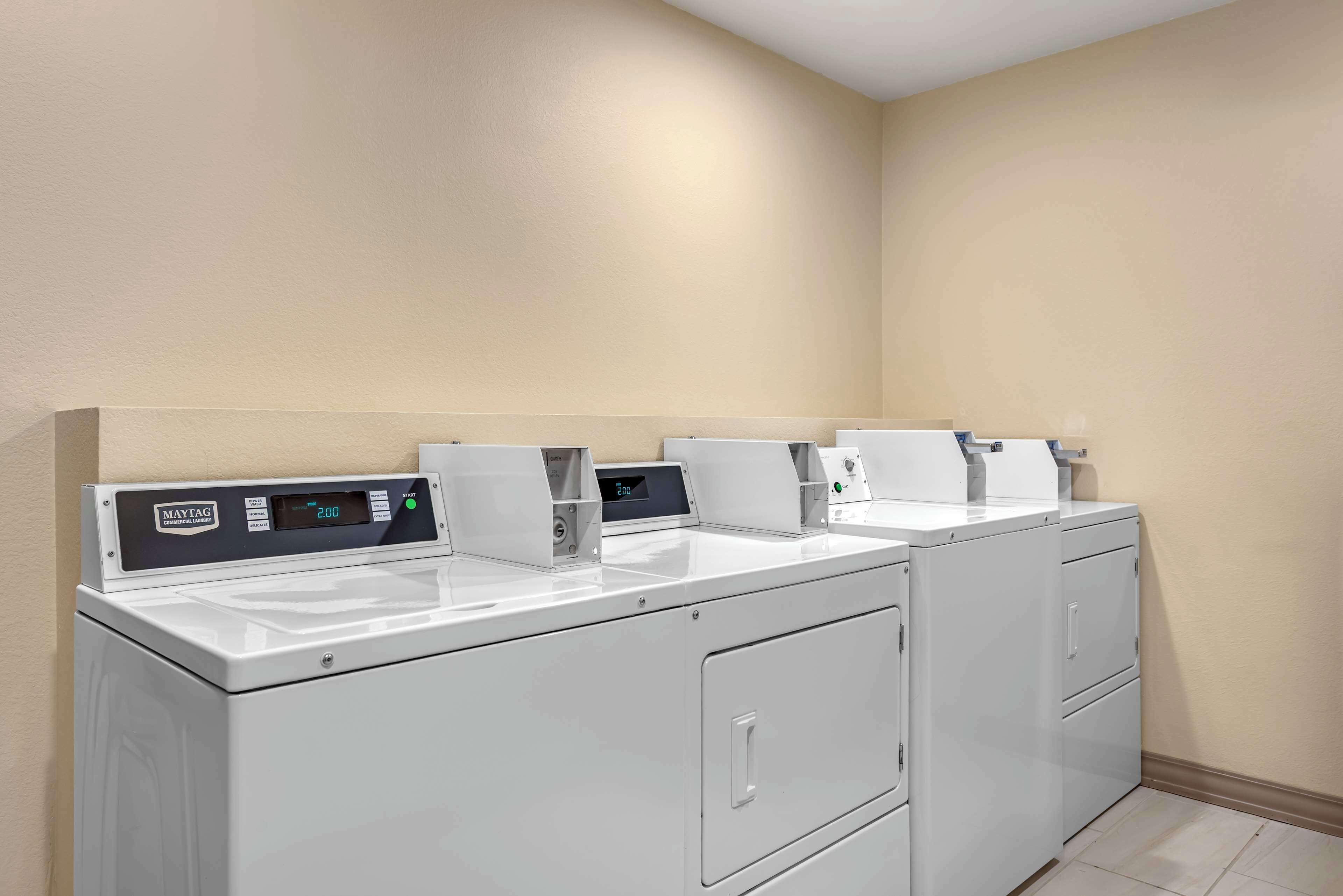 A row of Maytag front-loading washers and dryers in a corner of a room with beige walls and tiled flooring.