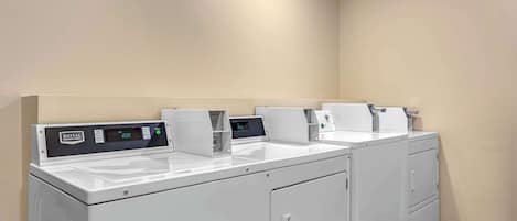 A row of Maytag front-loading washers and dryers in a corner of a room with beige walls and tiled flooring.