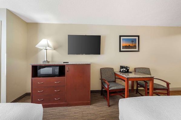 A hotel room with a bed, a desk with a lamp, a television, and a framed picture on the wall.