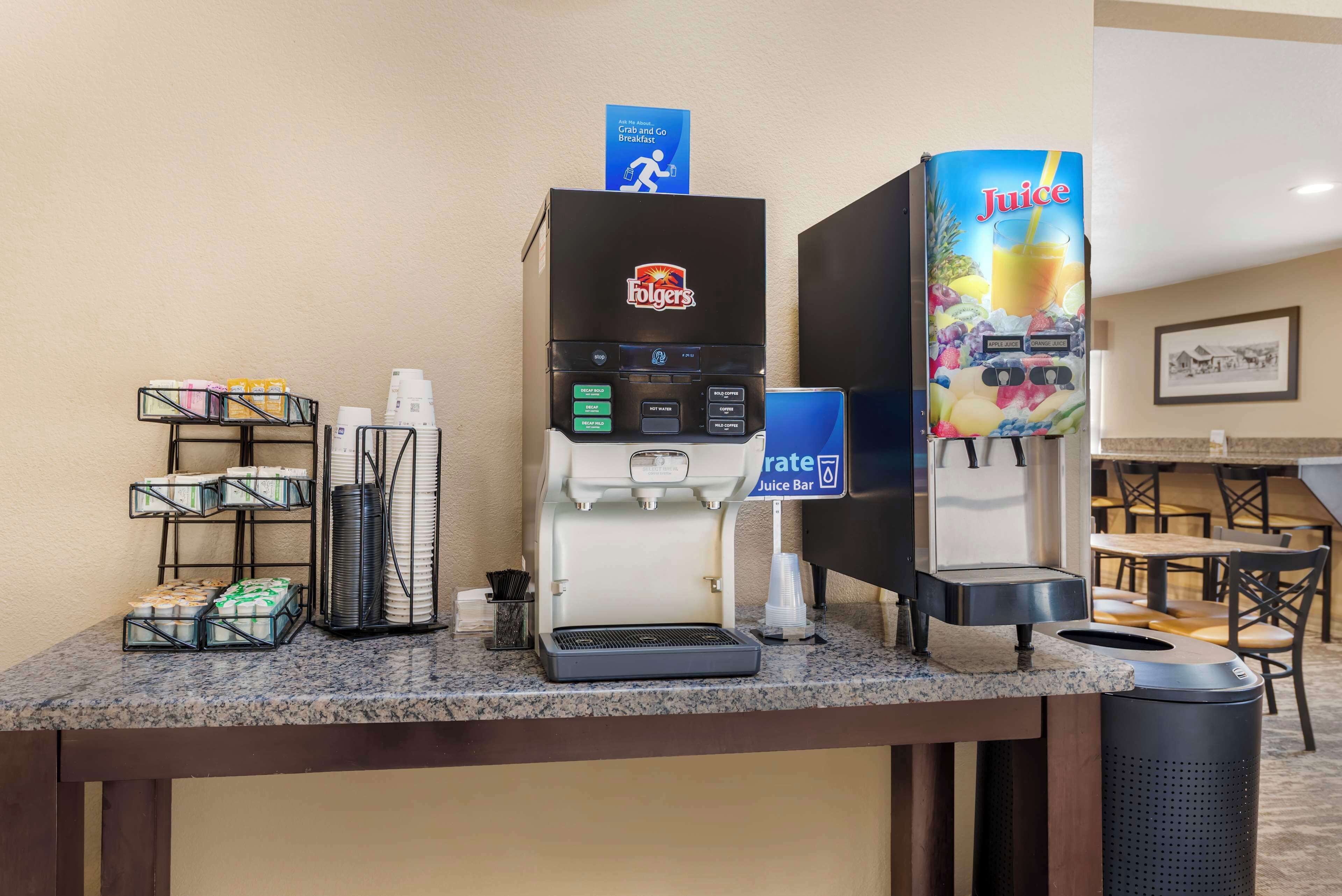 Un bar à jus proposant du café Folgers et des distributeurs de jus, des gobelets jetables, ainsi qu’un panneau indiquant qu’on peut y acheter un petit-déjeuner à emporter.
