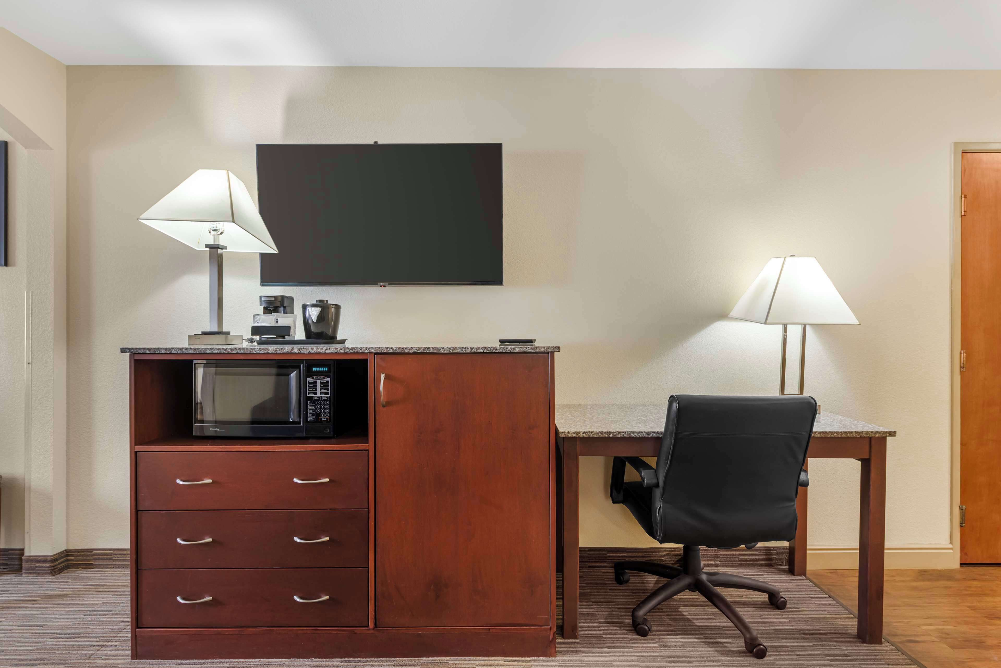 A hotel room with a kitchenette, a desk with a chair, and two lamps.