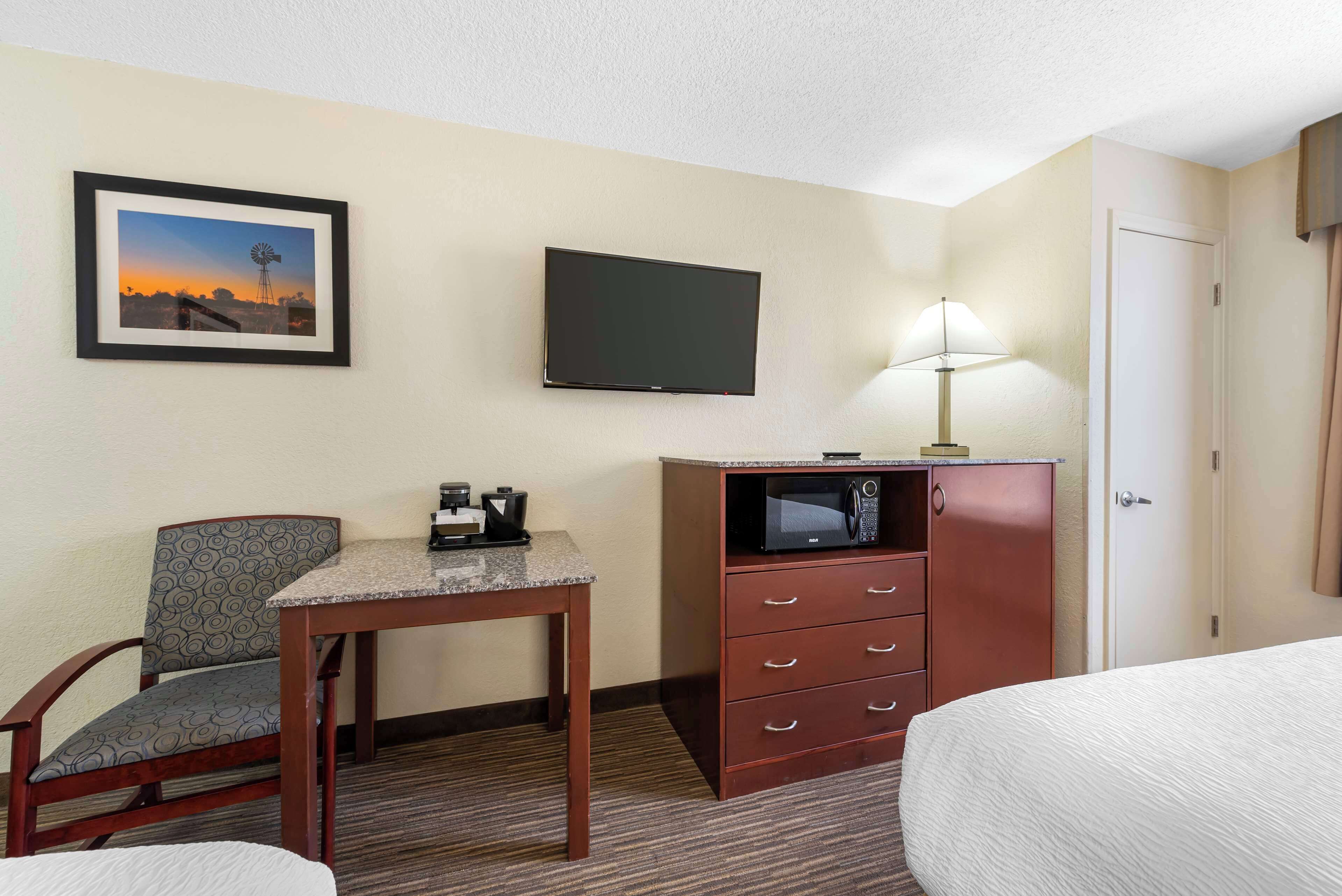 A hotel room with a bed, a desk with a chair, a television, a microwave, and a door.