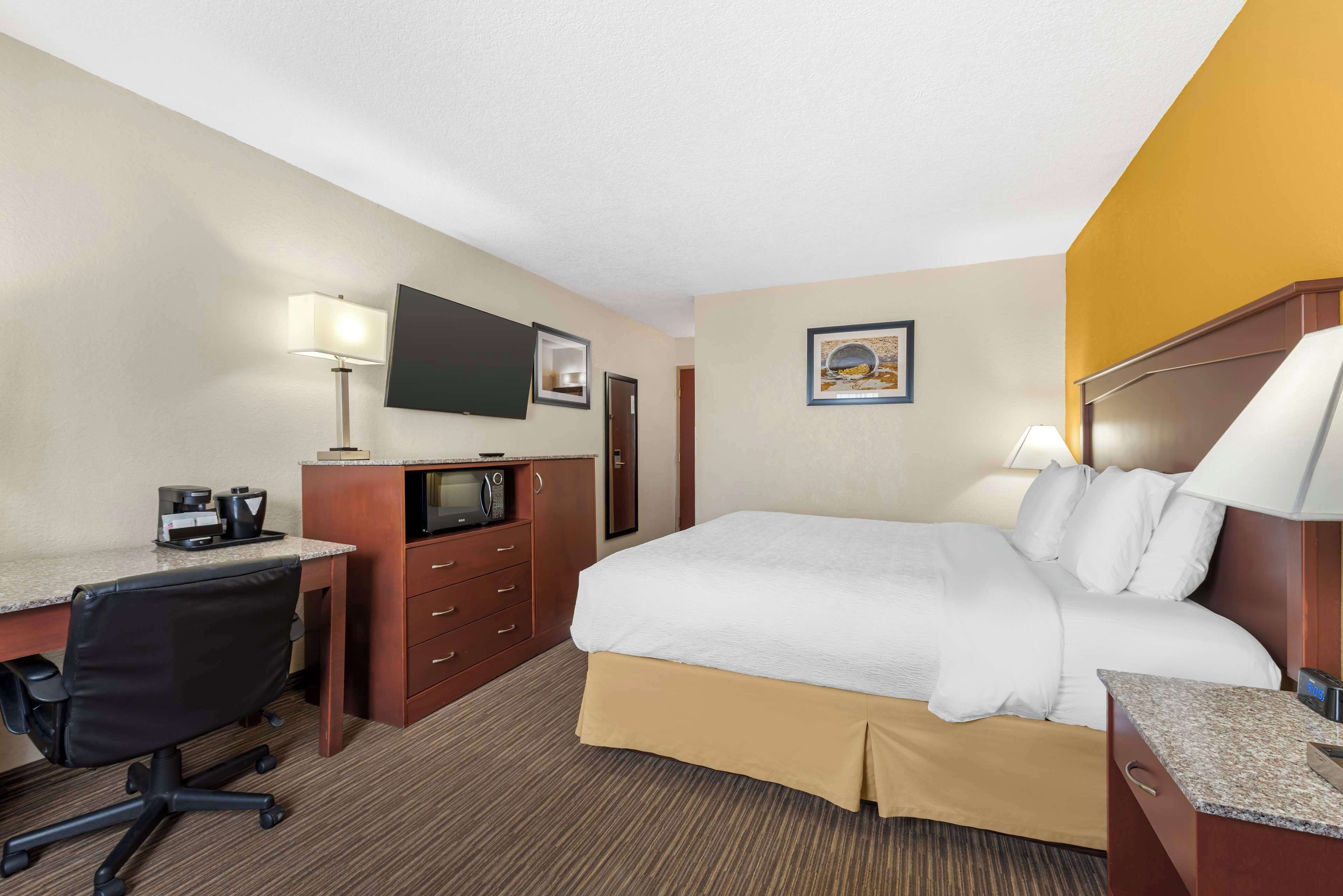 A hotel room with a bed, desk, chair, TV, and a painting on the wall.