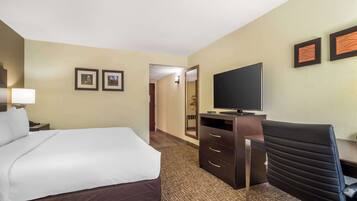 A hotel room with a bed, a desk with a television, and a chair. There are two framed pictures on the wall.
